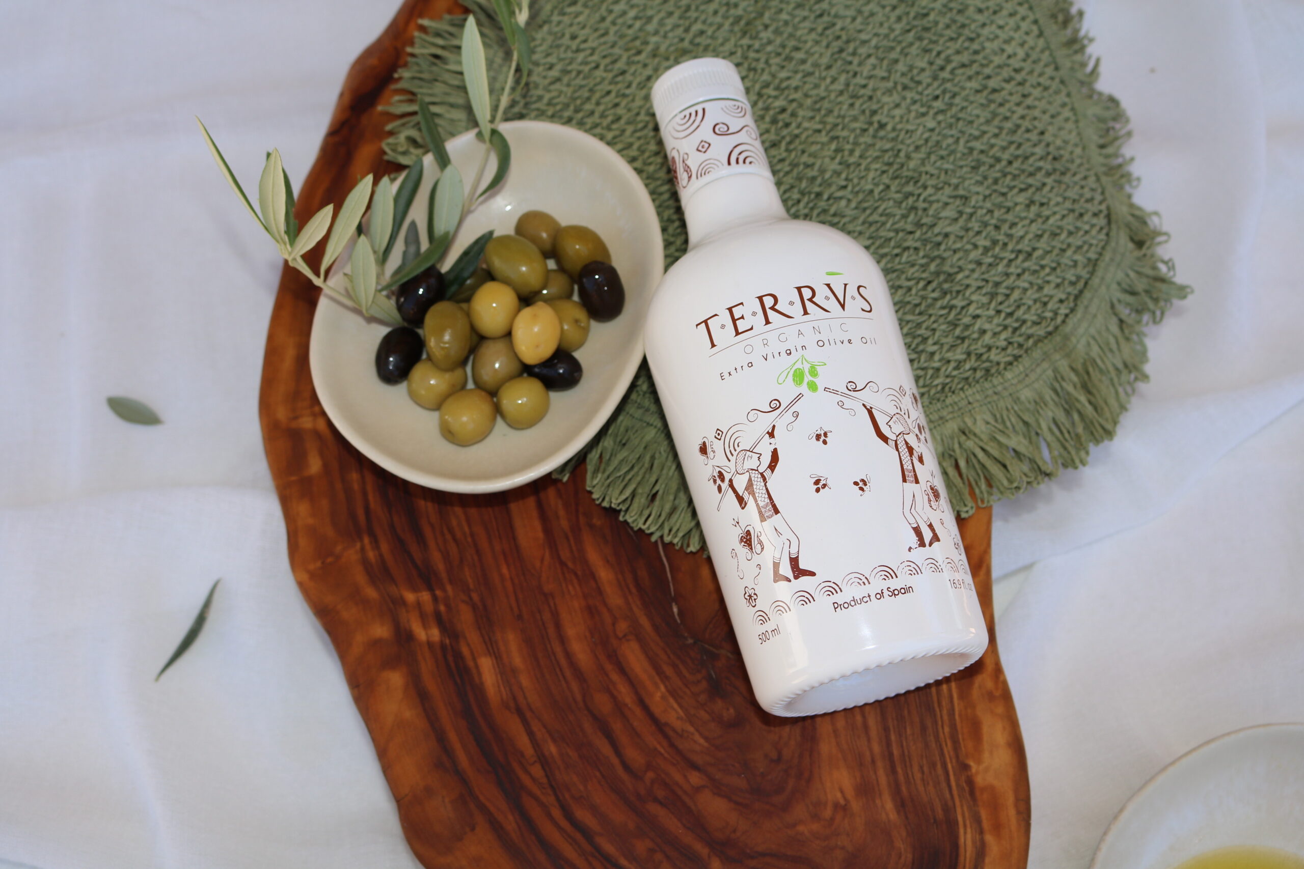 Botella de aceite de oliva virgen extra Terrvs junto a un plato con aceitunas verdes y negras sobre una tabla de madera.